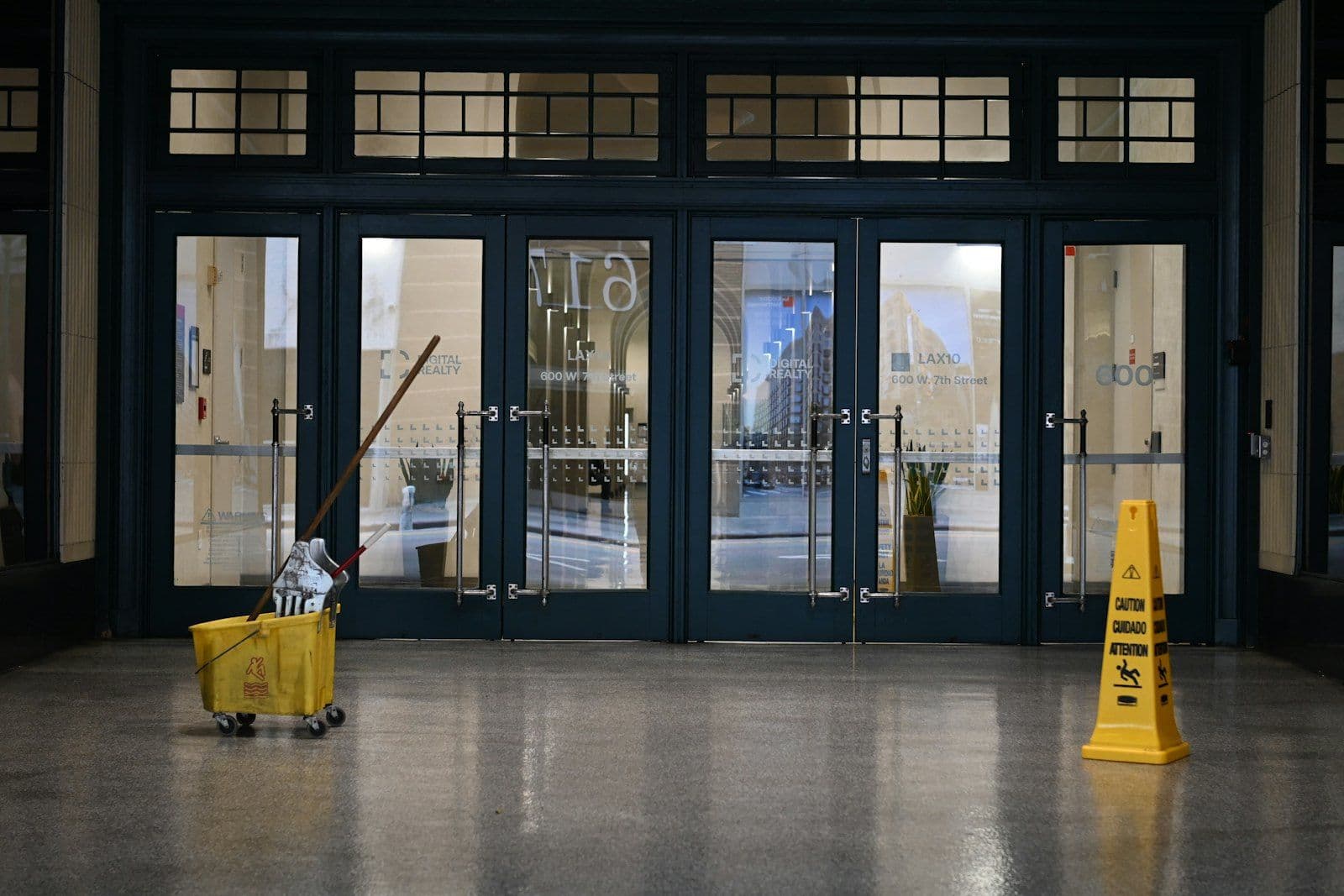 Commercial janitorial restoration of a glass-door office lobby with mop bucket and wet floor sign