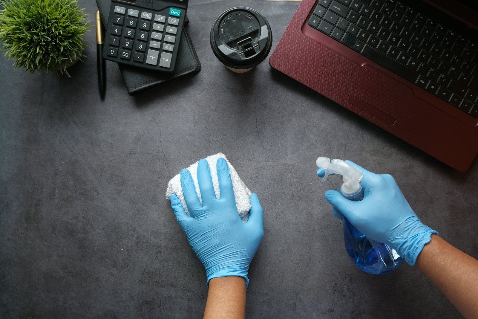 Janitorial cleaner in gloves disinfecting an office desk with spray and cloth, Houston TX
